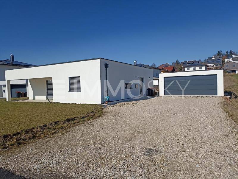 Modernes Einfamilienhaus mit integrierter Garage und Schotterauffahrt in ländlicher Umgebung.