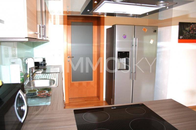 Moderne Küchenzeile mit Induktionskochfeld, Dunstabzugshaube und großem Kühlschrank.