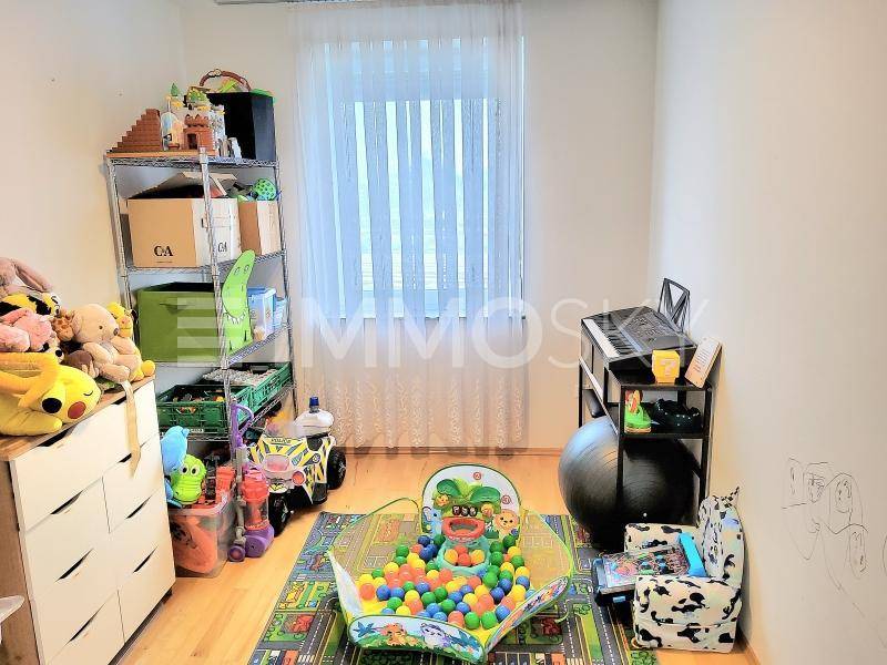 Kinderzimmer mit Spielzeug, Regalen und einem kleinen Schreibtisch am Fenster.