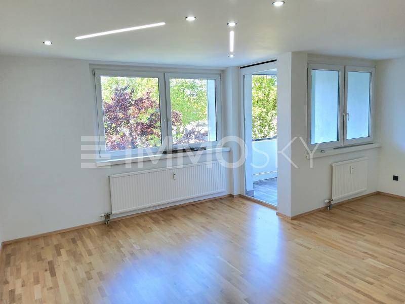 Helles Wohnzimmer mit Parkettboden, großen Fenstern und Zugang zum Balkon.