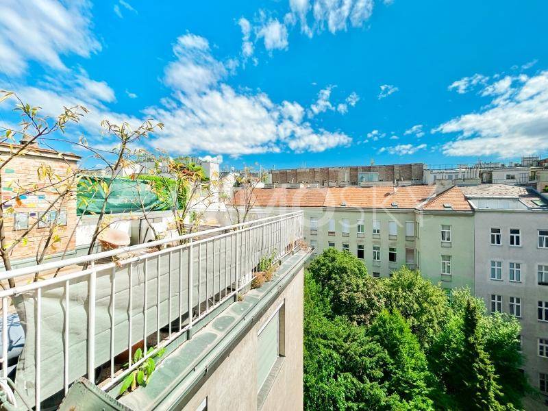 Blick von einem Balkon auf grüne Bäume und die umliegenden Gebäude der Stadt.