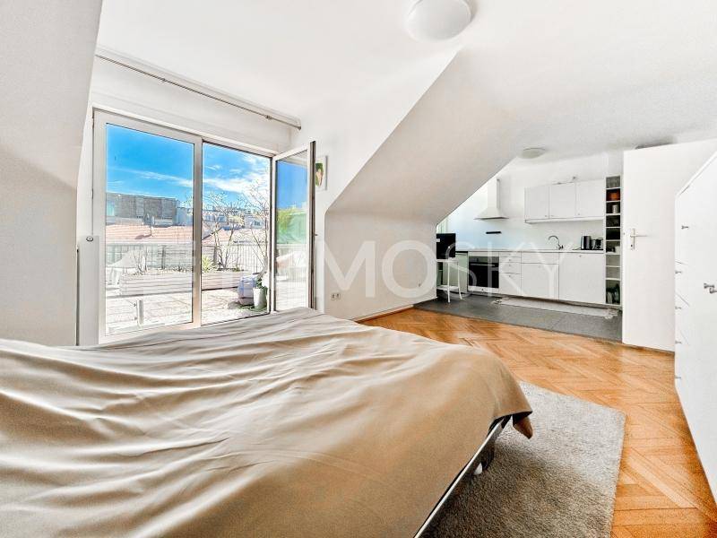 Helles Schlafzimmer mit Parkettboden, Zugang zur Dachterrasse und integrierter Küchenzeile.