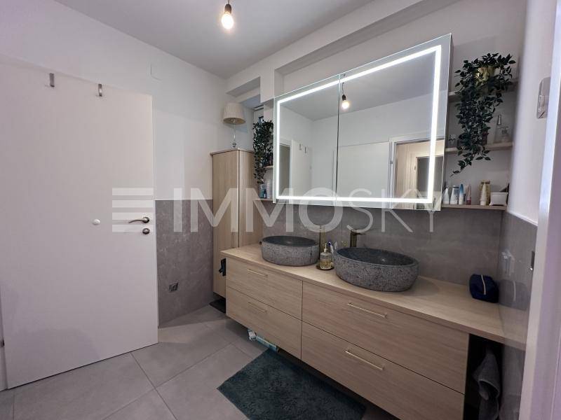 Modernes Badezimmer mit Doppelwaschbecken, beleuchtetem Spiegelschrank und großen Fliesen.