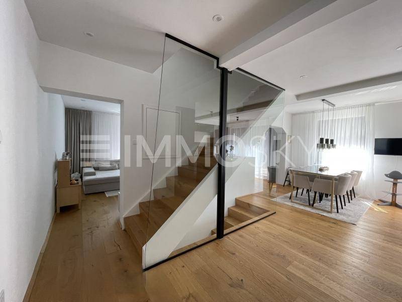 Offener Wohnbereich mit eleganter Holztreppe, Glasgeländer und Essbereich mit Holzboden.