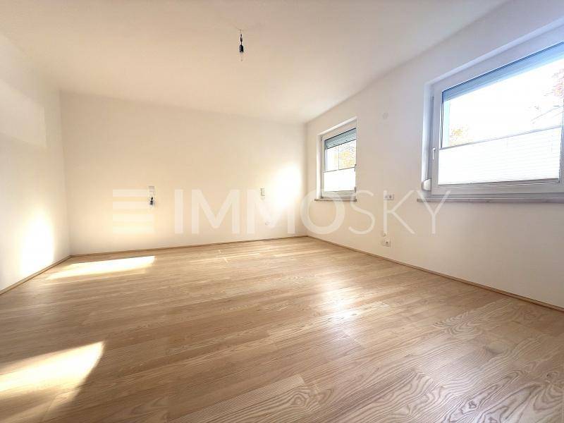 Geräumiges, unmöbliertes Zimmer mit hellem Parkettboden und zwei Fenstern, ideal als Schlafzimmer.