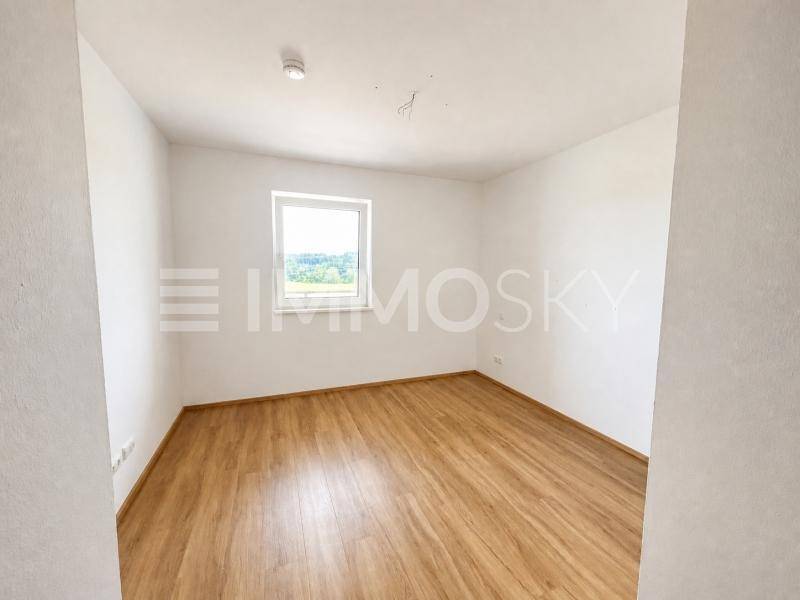 Helles Schlafzimmer mit Laminatboden und einem Fenster, das viel Tageslicht hereinlässt.