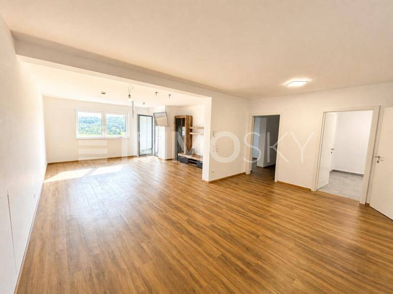 Geräumiger Wohnbereich mit Laminatboden, großen Fenstern und Zugang zu weiteren Räumen.