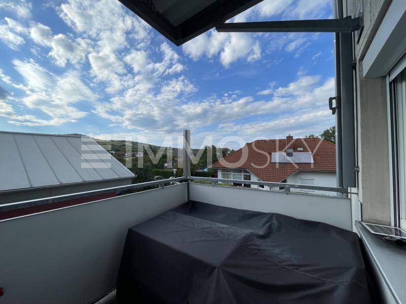 Balkon mit Blick auf die umliegende Landschaft und Wohngebäude unter blauem Himmel.