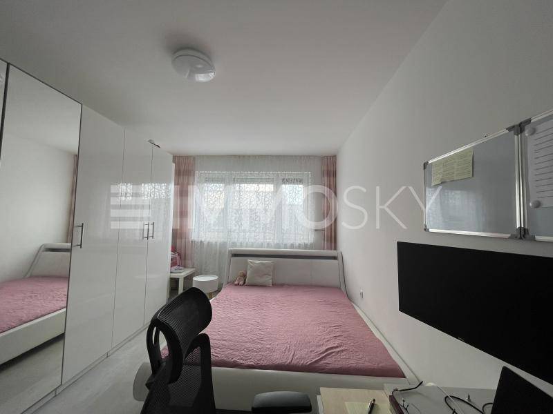 Helles Schlafzimmer mit Einzelbett, weißem Kleiderschrank und Schreibtisch am Fenster.