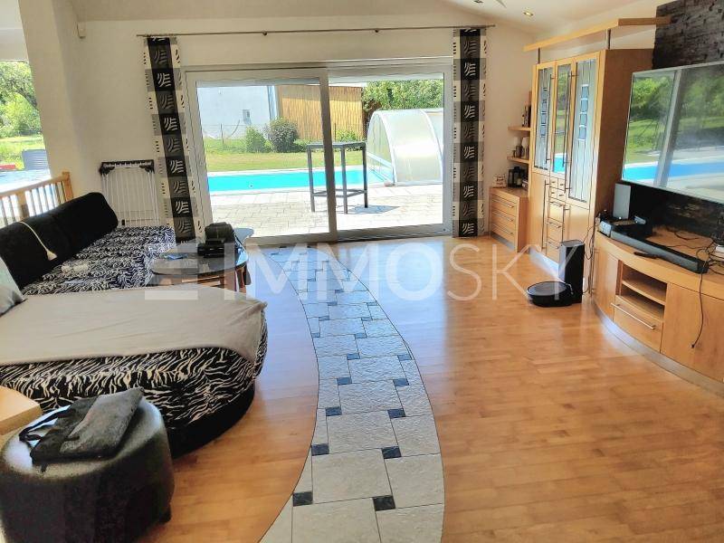 Geräumiges Wohnzimmer mit Holzboden, großem Sofa und direktem Zugang zum Poolbereich im Garten.