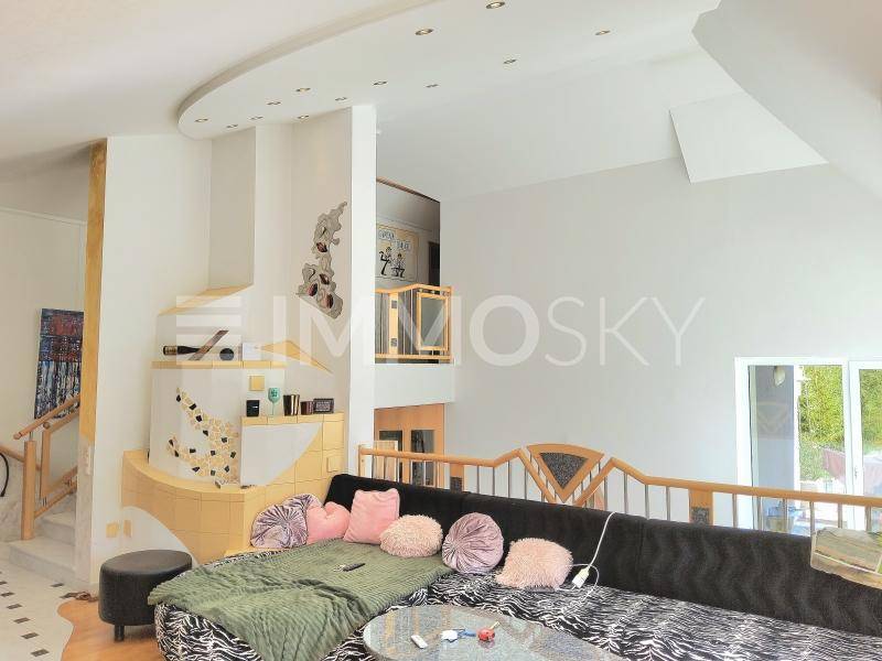 Helles Wohnzimmer mit modernem Kachelofen, großer Eckcouch und offener Galerie zum Obergeschoss.