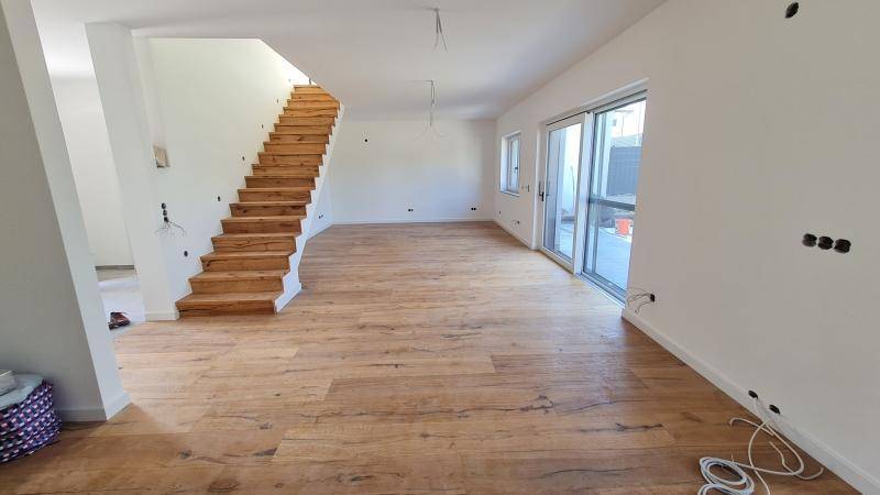 Heller Wohnbereich mit Holzboden und offener Holztreppe, bereit für den Innenausbau.