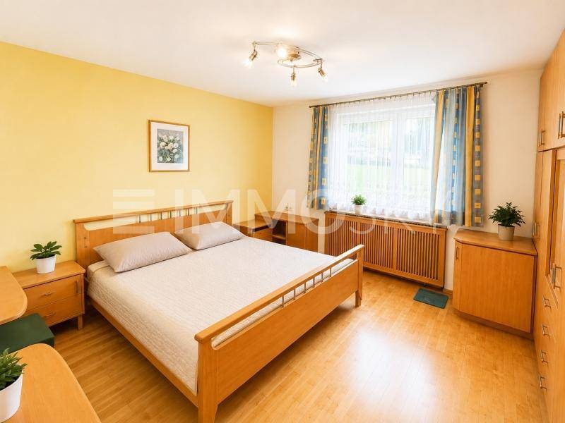 Schlafzimmer mit Doppelbett, Holzmöbeln, Parkettboden und Fenster mit Blick ins Grüne.