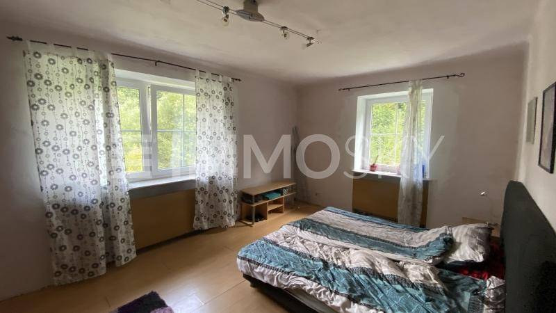 Helles Schlafzimmer mit zwei Fenstern, einem Doppelbett und schlichtem Bodenbelag.