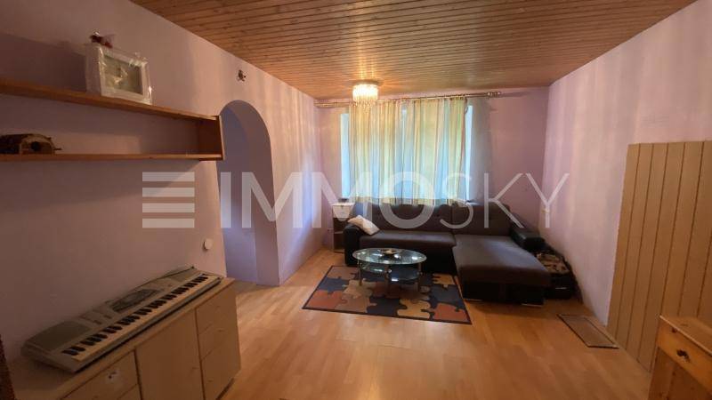 Gemütliches Wohnzimmer mit Ecksofa, Holzboden und einer Holztäfelung an der Decke.