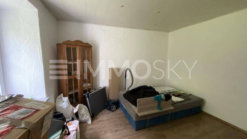 Schlichtes Schlafzimmer mit weißen Wänden, Laminatboden und einem Holzschrank, derzeit unaufgeräumt.