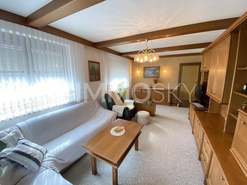 Gemütliches Wohnzimmer mit Teppichboden, Holzbalkendecke und traditionellen Möbeln.