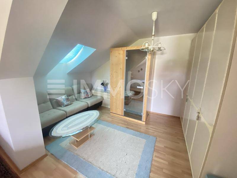 Gemütlicher Dachbodenraum mit Sofa, Teppich, Einbauschrank und einer kleinen Sauna unter einem Dachfenster.