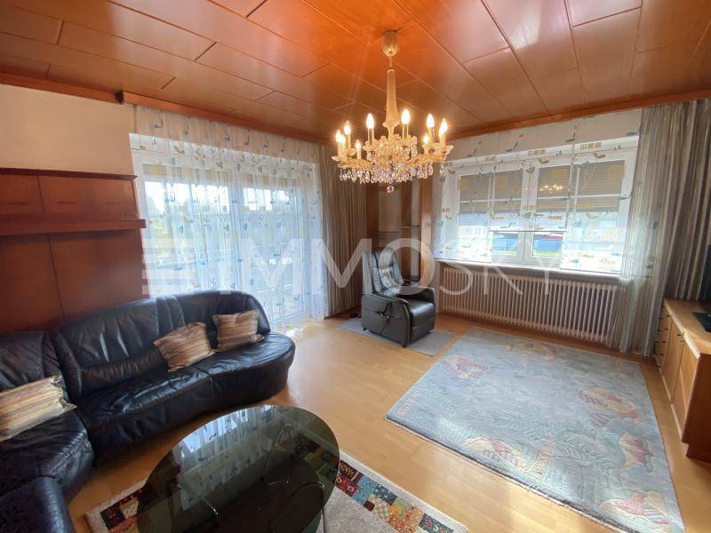Geräumiges Wohnzimmer mit dunklem Ledersofa, Holztäfelung an der Decke und einem großen Kronleuchter.