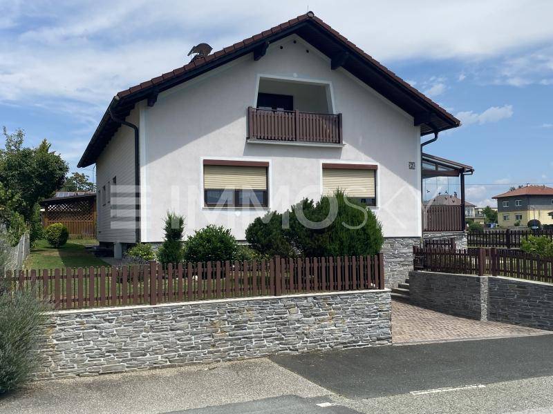 Einfamilienhaus mit Steinfassade im Sockelbereich, Balkon und gepflasterter Einfahrt.
