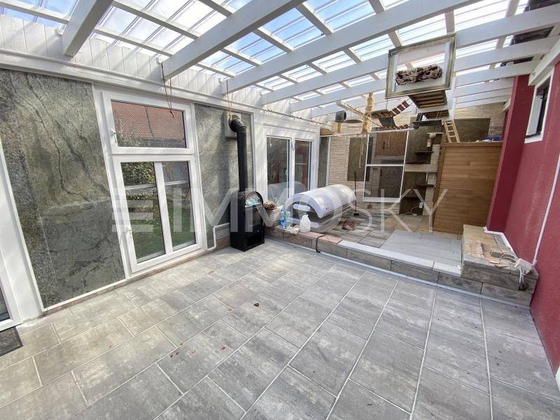 Heller Wintergarten mit Glasdach, Fliesenboden und einem Holzofen, ideal für Entspannung.