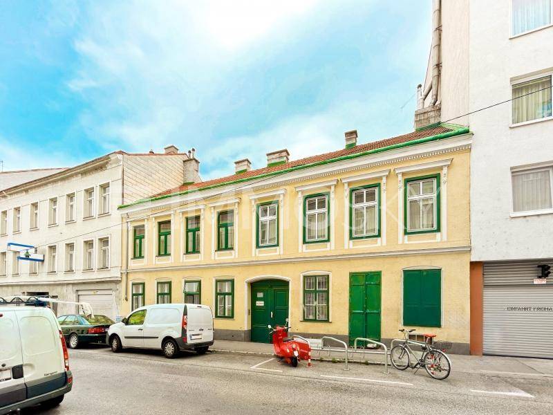 Historische Fassade eines Gebäudes mit gelbem Anstrich und grünen Fensterläden an einer belebten Straße.