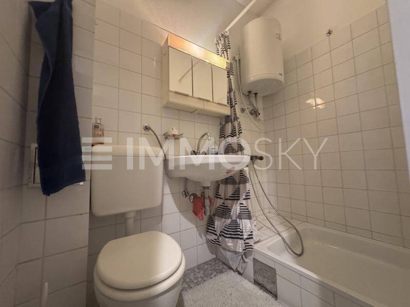 Funktionales Badezimmer mit weißen Fliesen, Badewanne und Waschbecken.