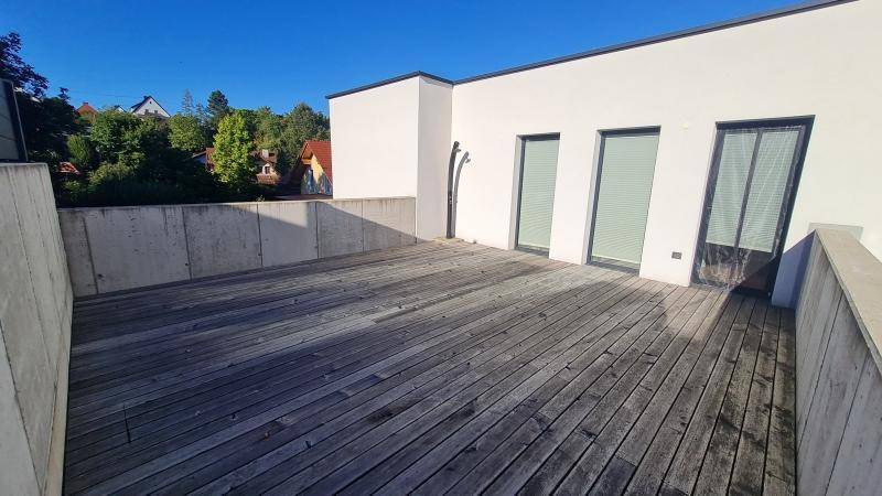 Geräumige Dachterrasse mit Holzdielenboden und Betonbrüstung unter blauem Himmel.