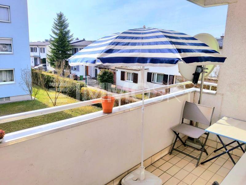 Balkon mit blau-weißem Sonnenschirm, Sitzgelegenheiten und Blick auf die Umgebung.