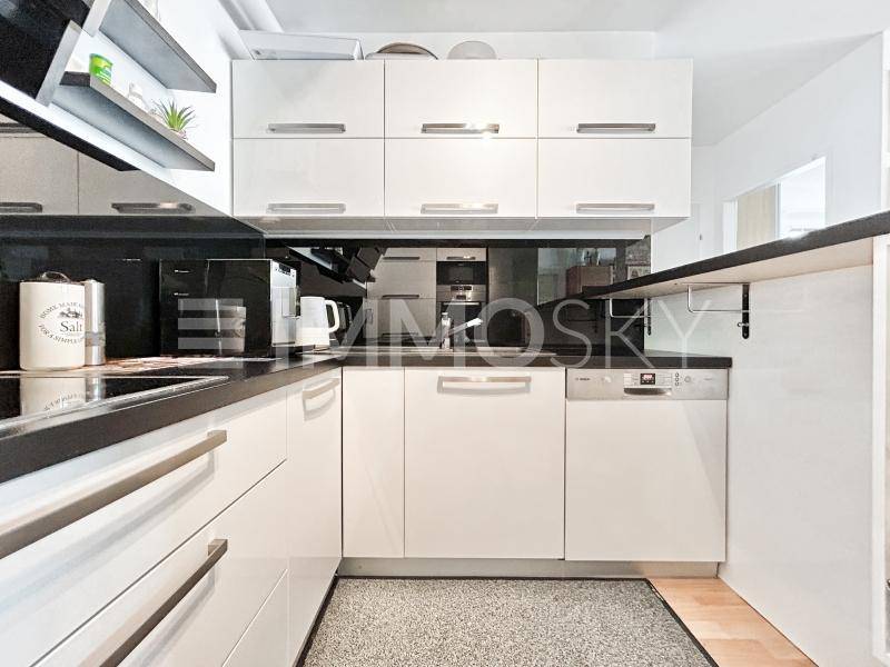 Moderne Küche mit weißen Hochglanzschränken, dunkler Arbeitsplatte und integriertem Geschirrspüler.
