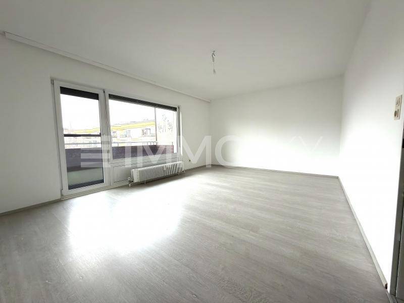 Heller, leerer Wohnraum mit modernem Laminatboden und großem Fenster mit Balkonzugang.