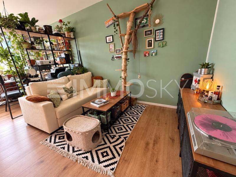 Helles Wohnzimmer mit beigem Sofa, grünen Wänden und vielen Pflanzen, inklusive Katzenbaum.