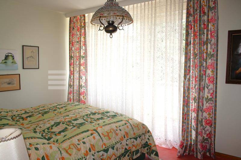 Schlafzimmer mit floralen Vorhängen, großem Fenster und gemütlichem Bett.