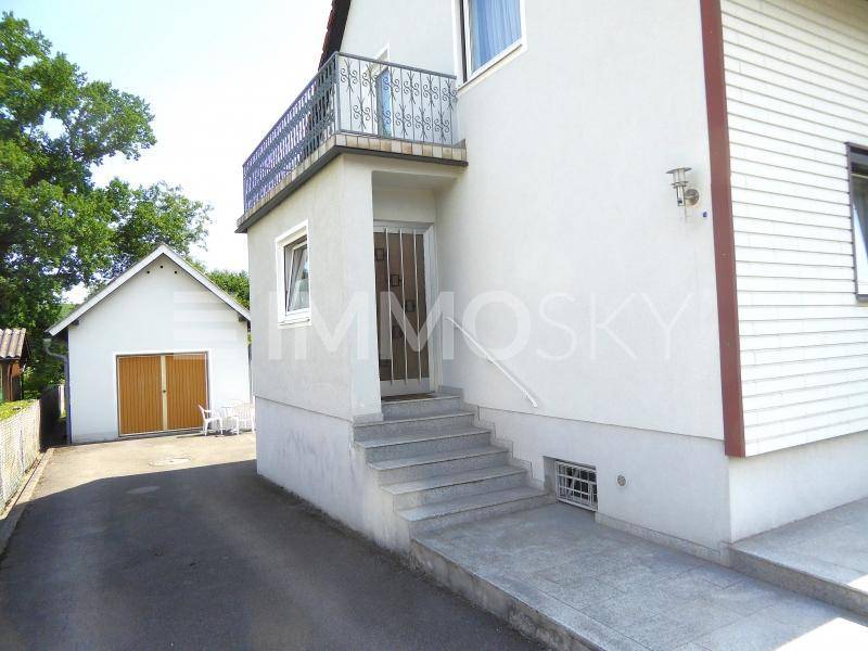 Detailansicht des Hauseingangs mit Treppe, Rampe und einem kleinen Balkon darüber.