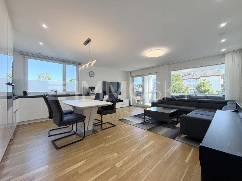 Heller offener Wohn-Essbereich mit moderner Küche, Holzboden und Zugang zum Balkon.
