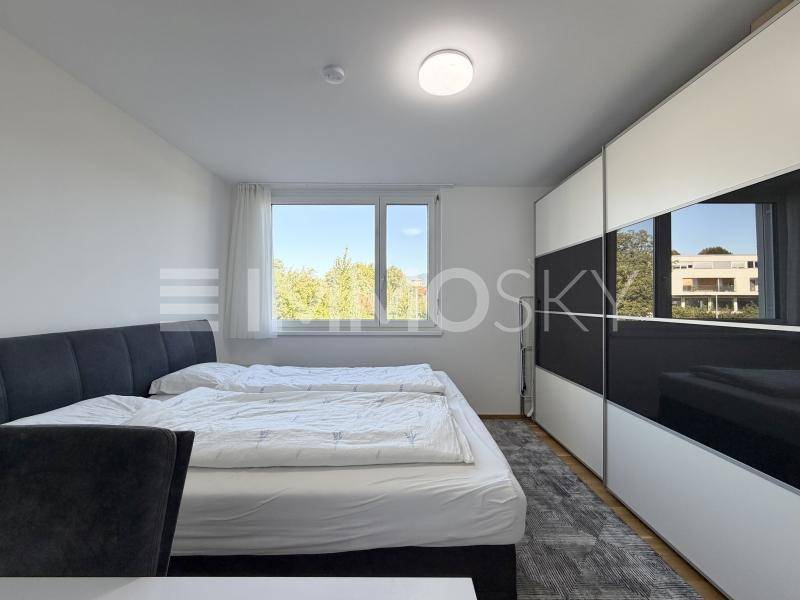 Helles Schlafzimmer mit Doppelbett, großem Fenster und modernem Einbauschrank.