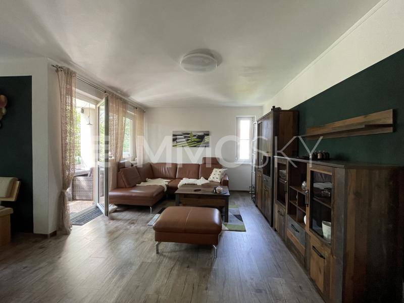 Geräumiges Wohnzimmer mit bequemer Ledercouch, Holzboden und Zugang zum Balkon.
