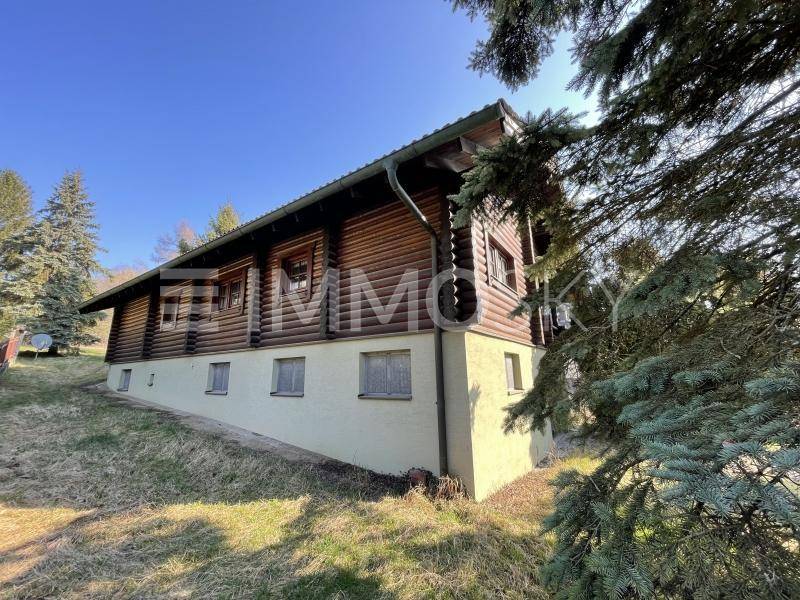 Holzhaus im Chalet-Stil mit Blockbauweise und hellem Sockelgeschoss, umgeben von Bäumen.