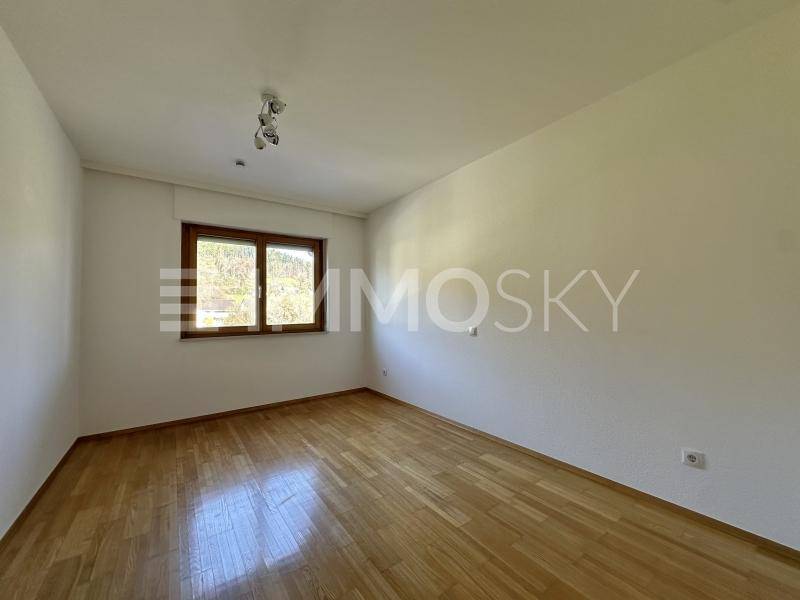 Ruhiges Schlafzimmer mit Holzparkettboden und einem Fenster, das viel Tageslicht hereinlässt.