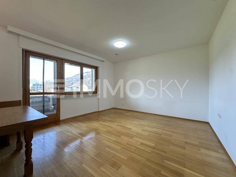 Helles Wohnzimmer mit Parkettboden und Zugang zu einem Balkon, bietet viel natürliches Licht.