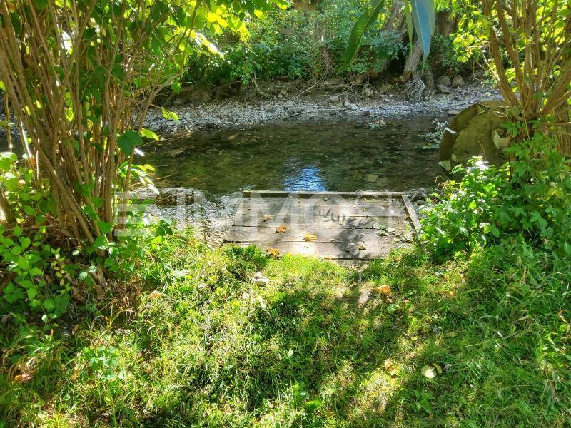 Kleiner Bachlauf mit Holzsteg und üppiger Vegetation am Ufer.