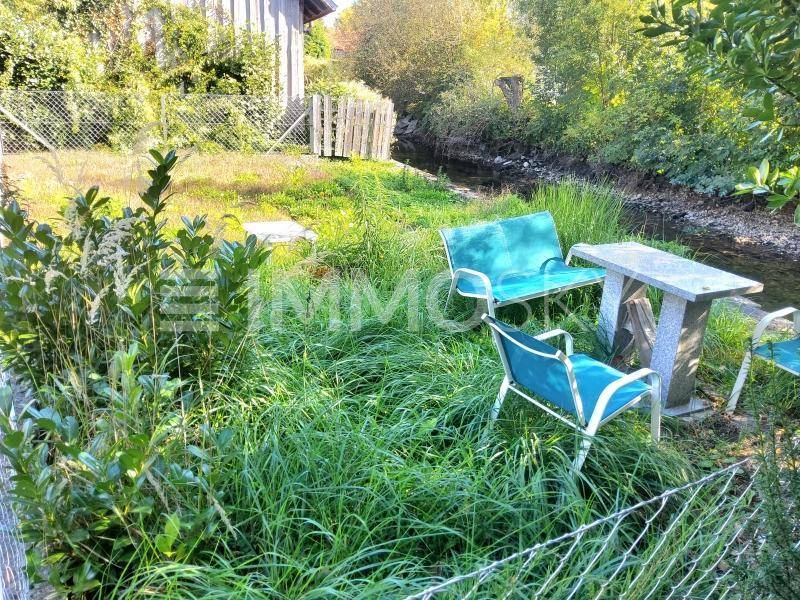 Gemütlicher Sitzbereich am Bachlauf mit Tisch und Stühlen im Grünen.