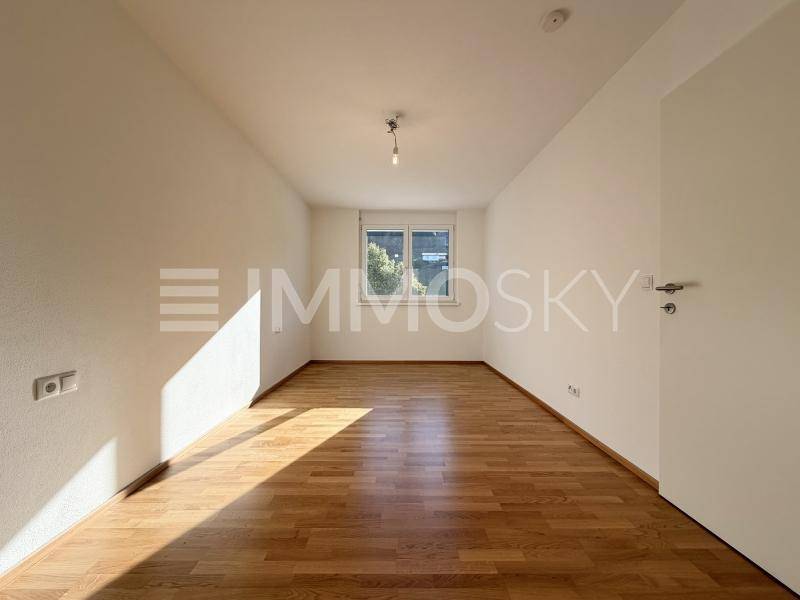 Leeres Schlafzimmer mit hellem Holzboden und einem Fenster, das viel Tageslicht hereinlässt.