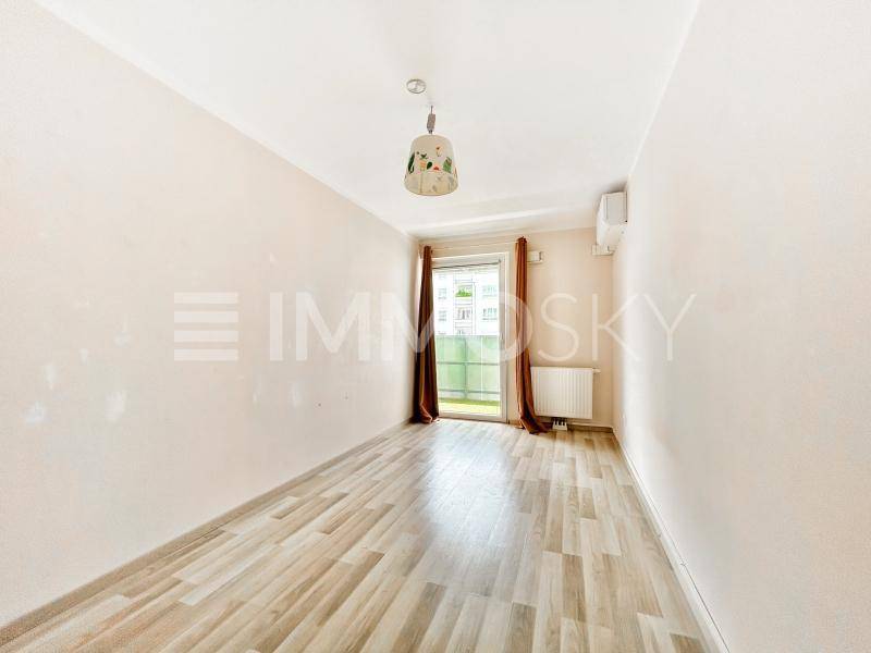 Leeres Zimmer mit Laminatboden in Holzoptik, weißen Wänden und einem Fenster mit Vorhängen.