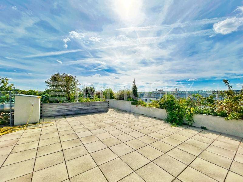 Geräumige Dachterrasse mit Fliesenboden, Pflanzen und weitem Blick über die Stadtlandschaft.
