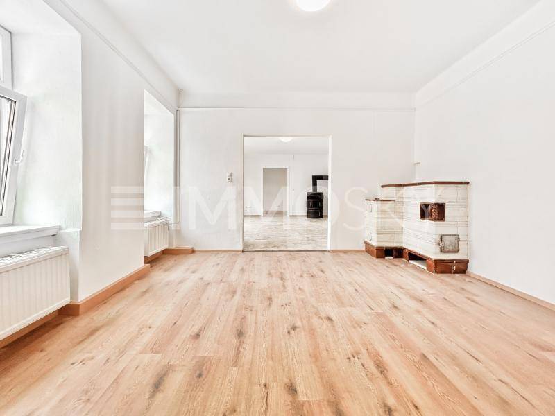 Heller Raum mit Holzboden, weißen Wänden und einem traditionellen Kachelofen.