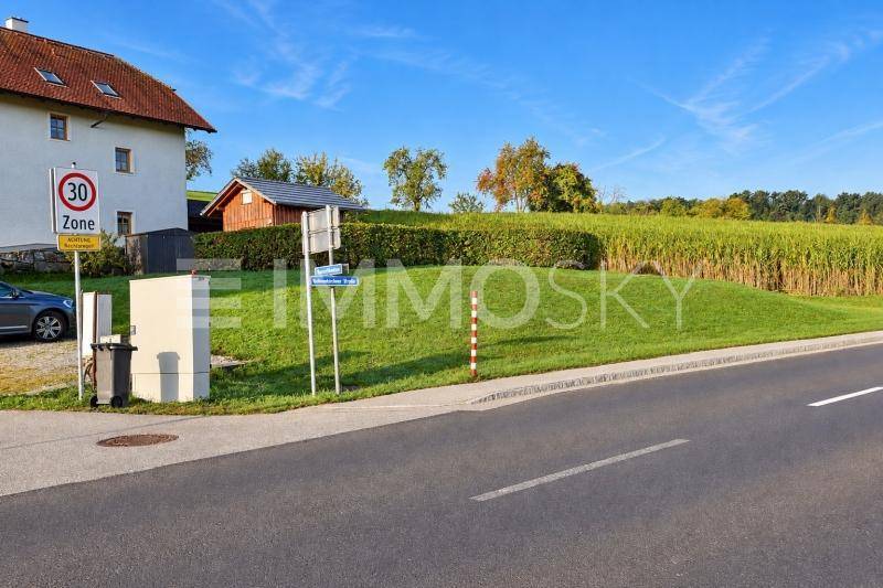 Blick von der Straße auf das Grundstück mit einem Haus, Holzschuppen und angrenzendem Feld.