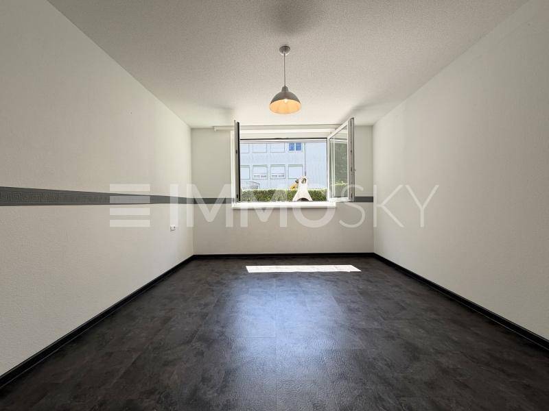 Leeres Zimmer mit dunklem Bodenbelag und einem großen Fenster für viel Tageslicht.