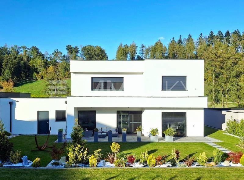 Moderne weiße Villa mit Flachdach, gepflegtem Garten und möblierter Terrasse im Grünen.