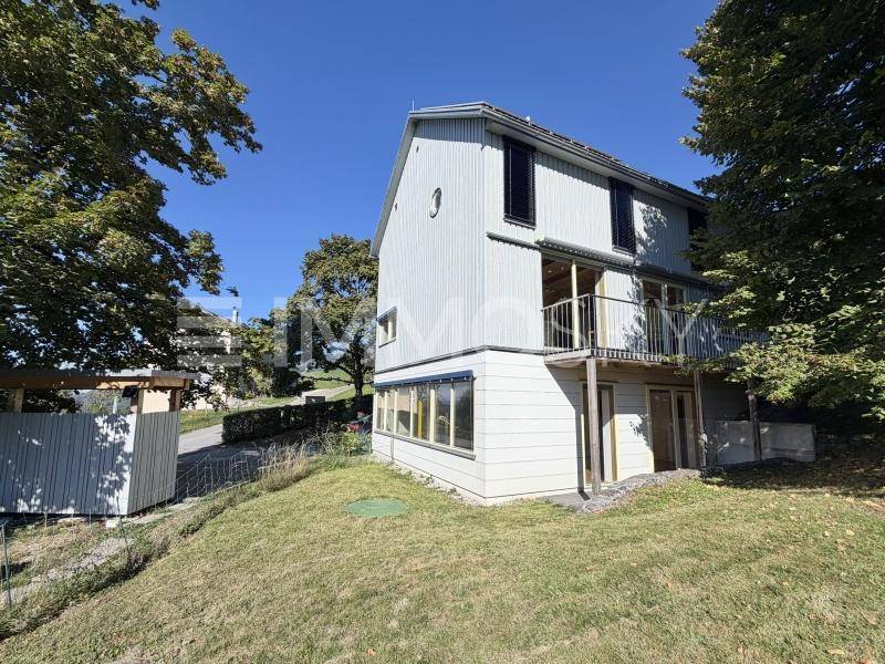 Seitliche Ansicht eines Hauses mit Holzverkleidung, Balkon und Gartenbereich.